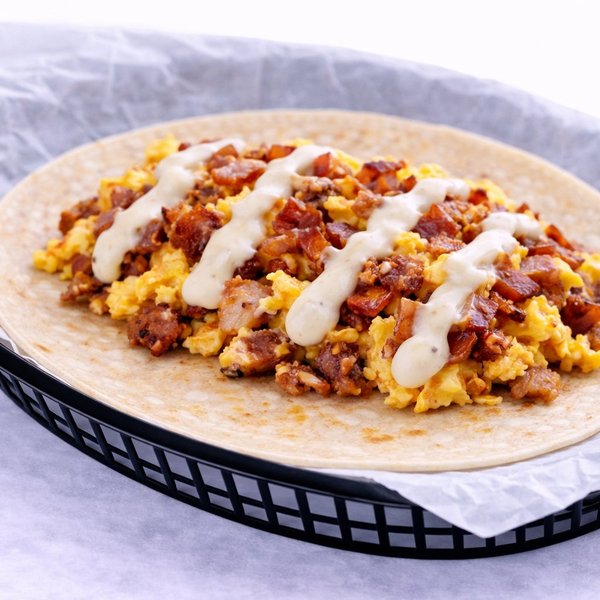 Bacon and egg breakfast taco drizzled with signature queso on a flour tortilla